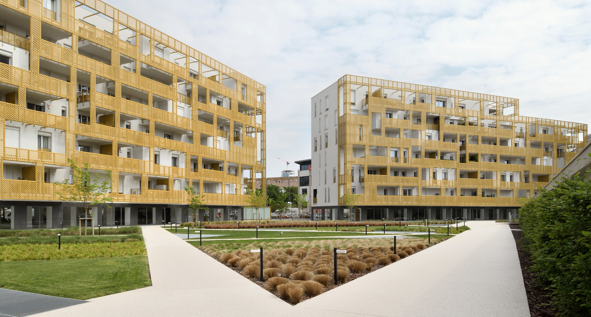 Modern residential complex with wooden-clad facades and balconies surrounding a landscaped courtyard with pathways and ornamental grasses.