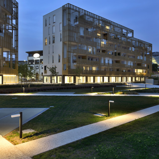 Artemide bollard lights illuminate a modern residential complex pathway and green areas at dusk, creating a warm, welcoming outdoor ambiance.