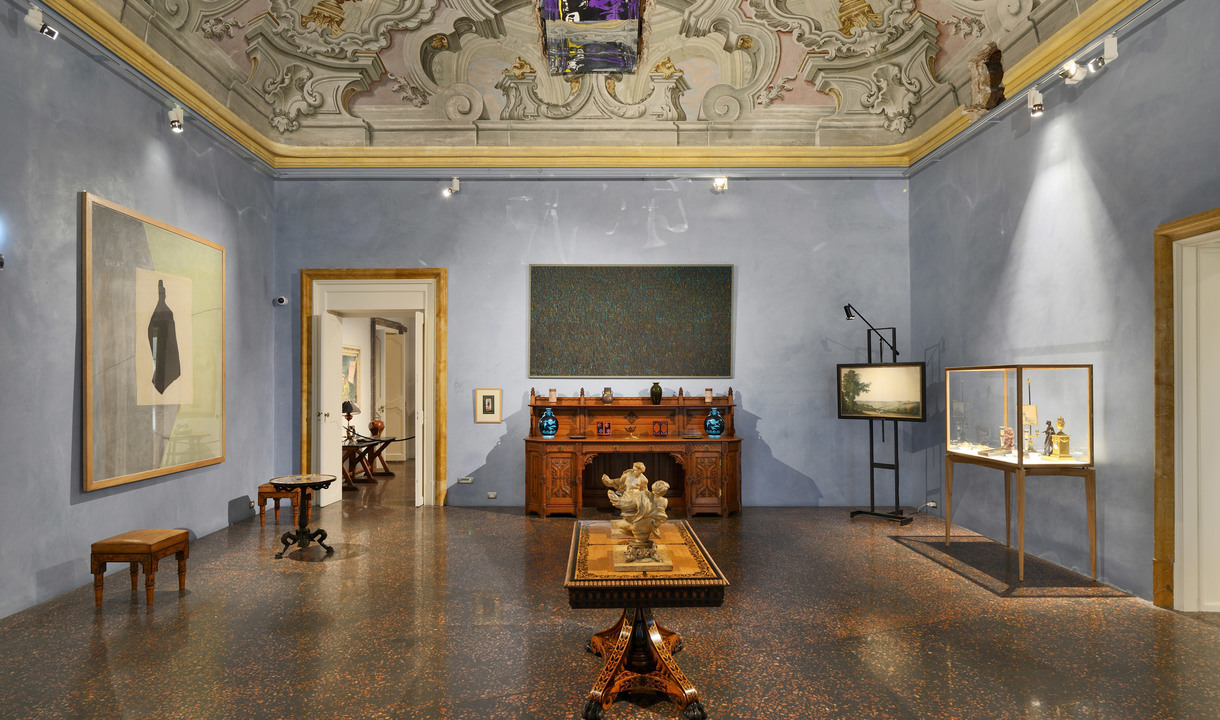 Elegant museum room with frescoed ceiling, blue walls, antique furniture, artworks, display cases, and Artemide spotlights illuminating exhibits.