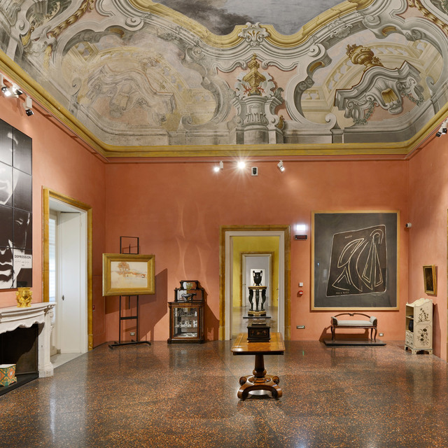 Baroque frescoed ceiling room with salmon walls, track spotlights illuminating artworks, antique furniture, and a polished terrazzo floor.