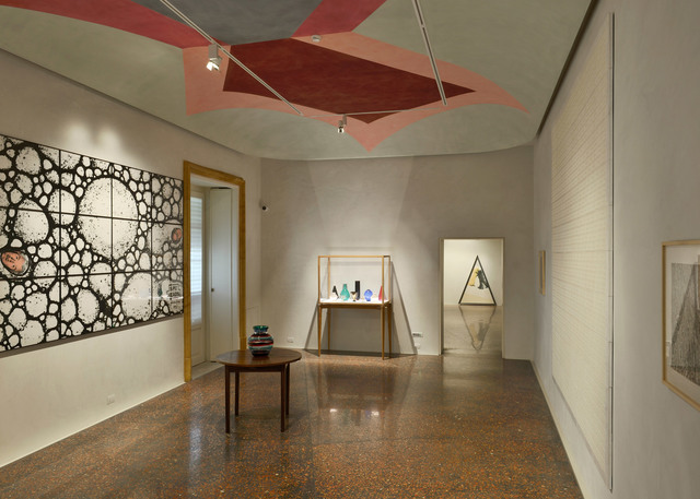 Gallery interior with polished terrazzo floor, artwork on walls, display case with glass objects, and track spotlights on a painted ceiling.