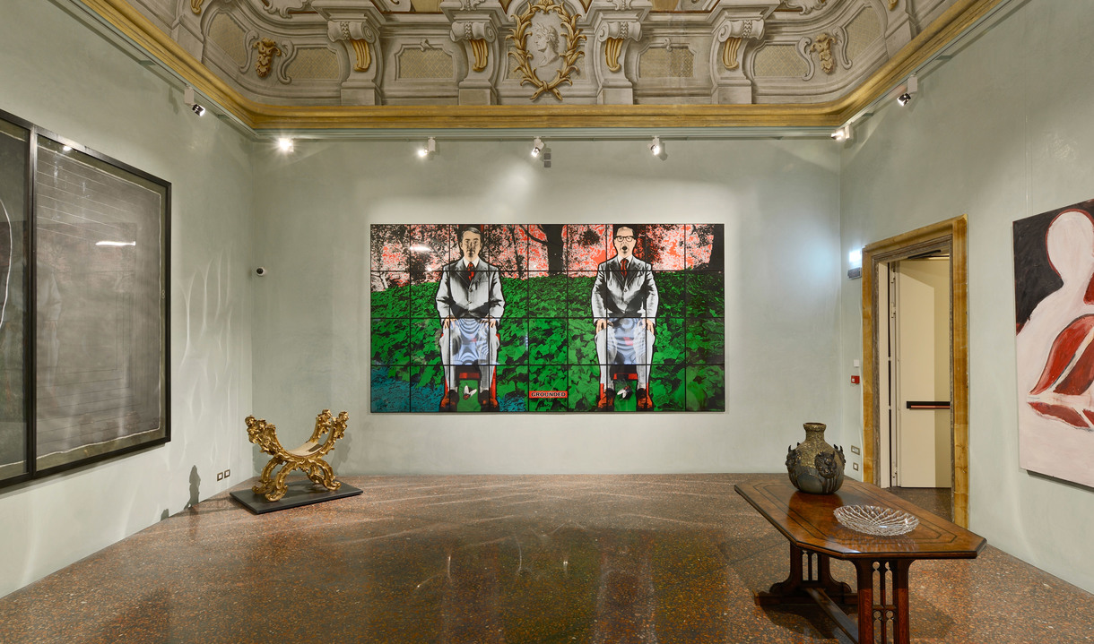 Art gallery in ornate room with frescoed ceiling, track spotlights illuminating large paintings and sculptures on marble floor.