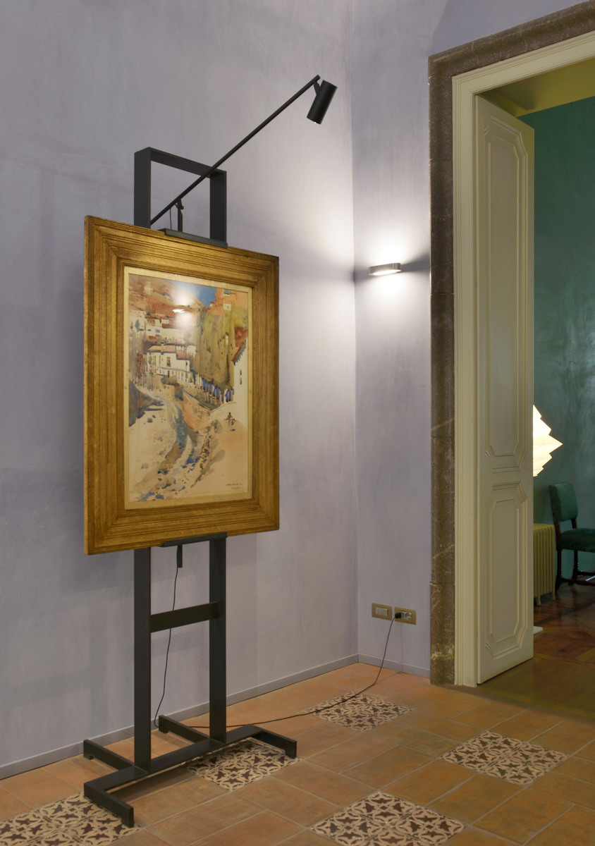 Artemide adjustable black picture light on easel illuminating a framed painting in a classic interior with terracotta floor