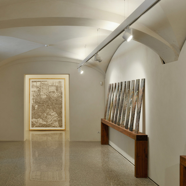 Art gallery with vaulted ceiling lit by Artemide track spotlights, illuminating large artwork and sculptural installation on wooden bench
