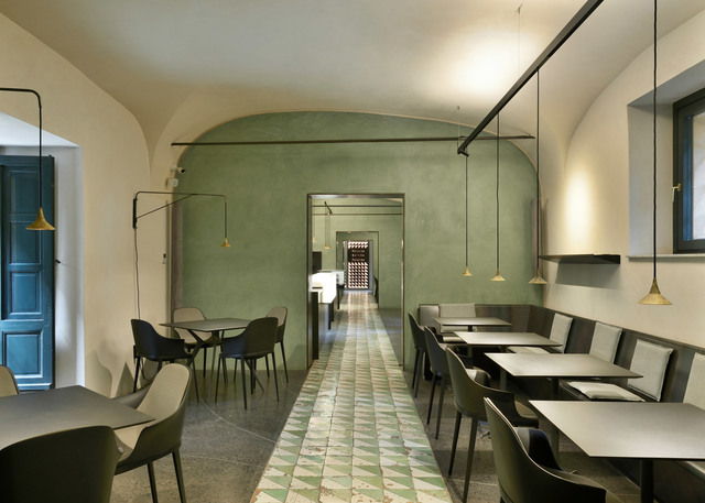 Restaurant interior with arched ceilings, green walls, and brass conical pendant lights illuminating dark tables and chairs.