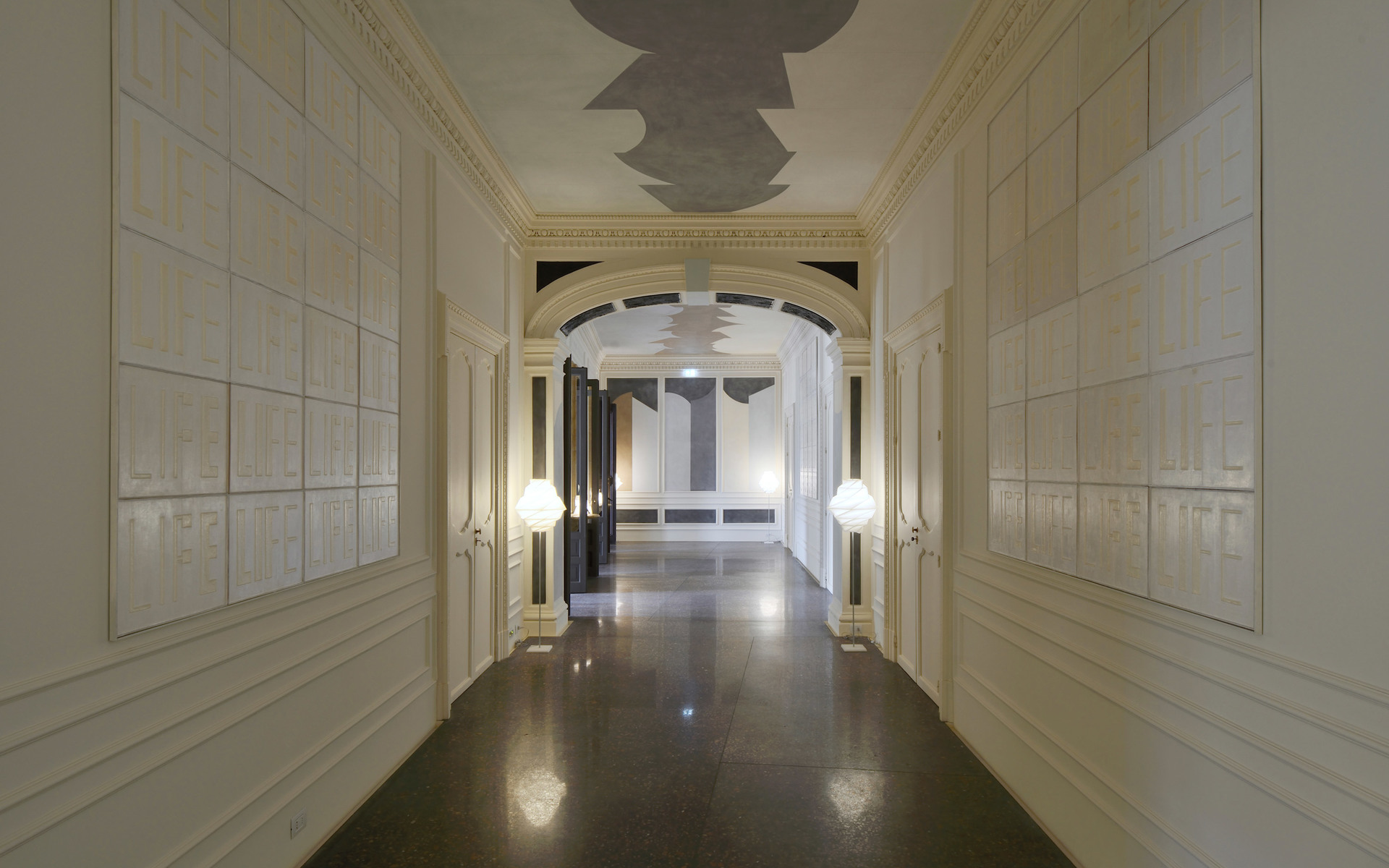 Elegant corridor with classical architecture, illuminated by two spherical white floor lamps flanking a grand archway with dark marble floors.