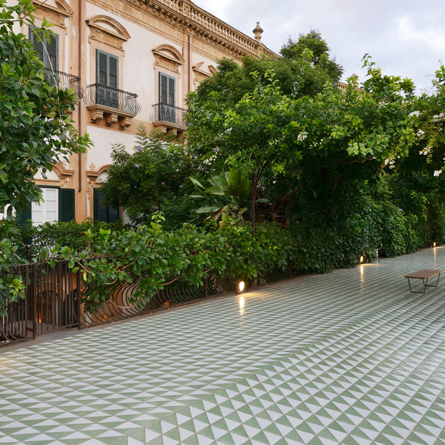 Outdoor courtyard of a historic villa with geometric green-white tiled floor, lush garden, and Artemide ground lights illuminating the path.