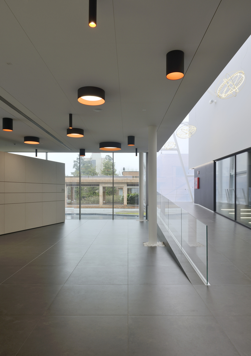 Modern corridor with multiple black cylindrical ceiling-mounted lights with warm golden interiors illuminating a bright open space.
