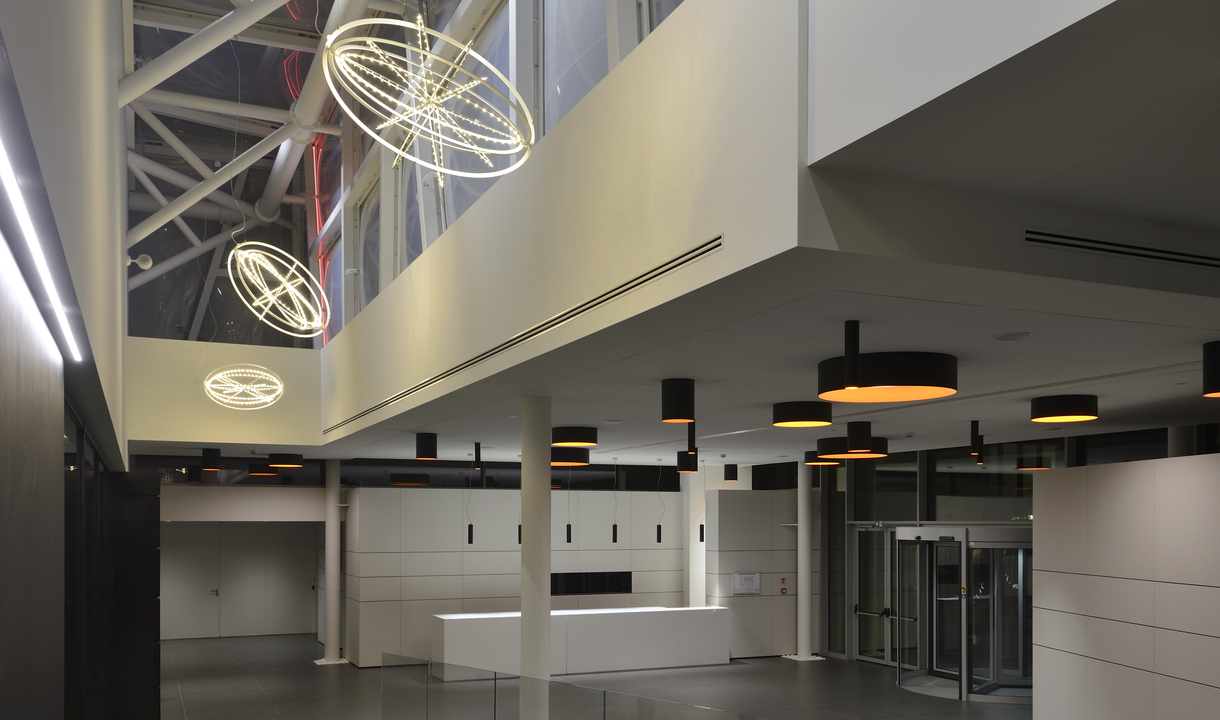 Modern lobby with Artemide orbital ring pendant lights and cylindrical black-gold ceiling fixtures illuminating a spacious entrance hall