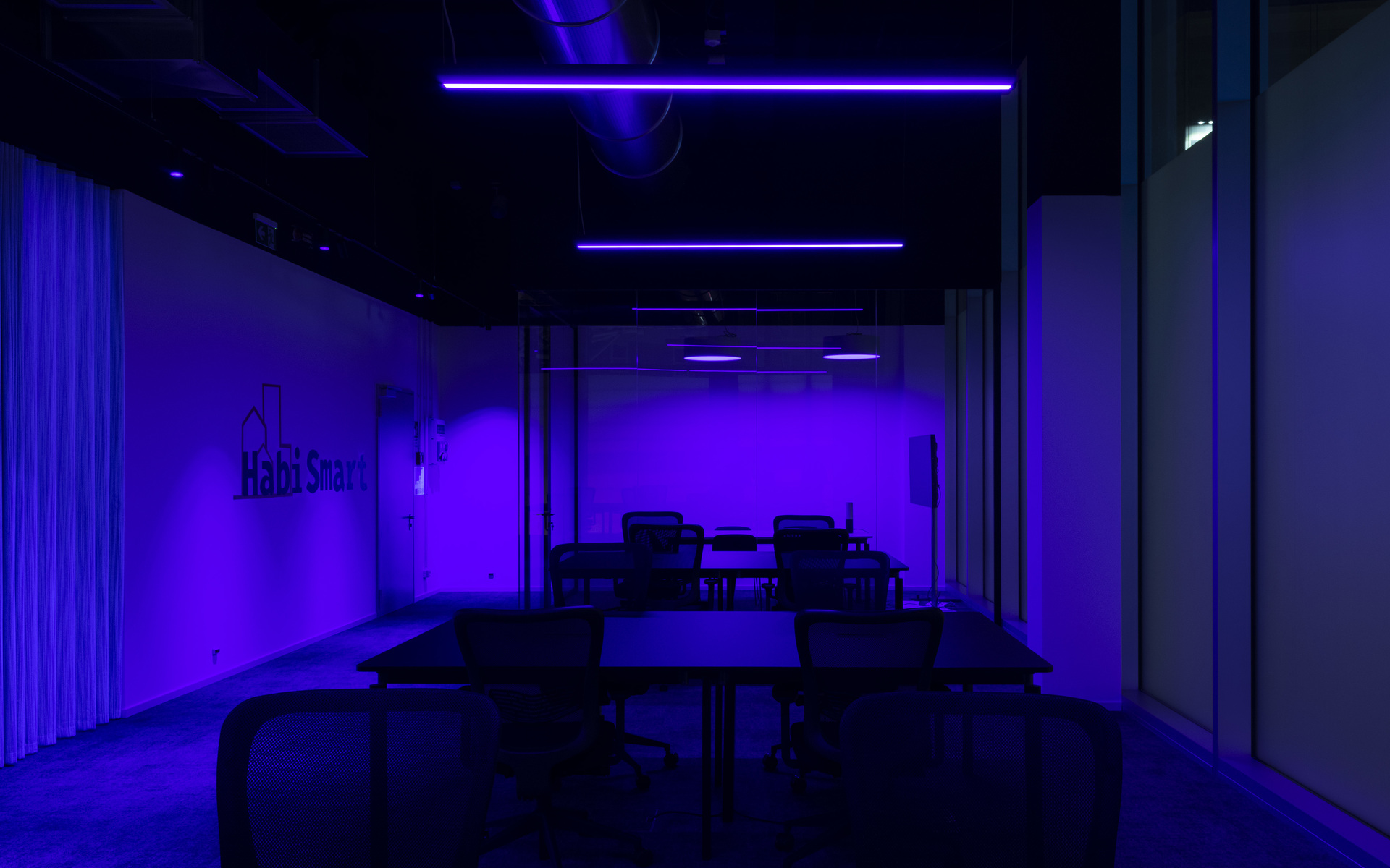 Dark meeting room bathed in vivid purple light from linear LED ceiling fixtures, with tables and chairs arranged in rows.