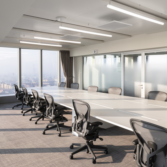 Modern conference room with a long white table, ergonomic chairs, and Artemide linear LED ceiling lights providing uniform illumination.