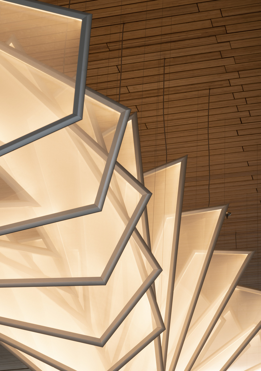 Large architectural ceiling installation with fan-shaped luminous panels framed in metal, emitting warm white light against a wood-paneled ceiling