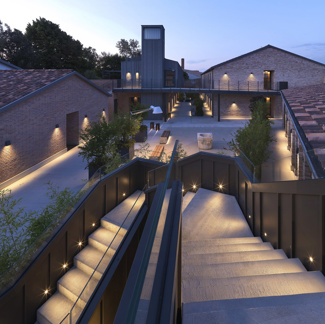 Dusk view of a brick courtyard complex with illuminated staircases, step lights, and wall-mounted fixtures creating warm ambient lighting.