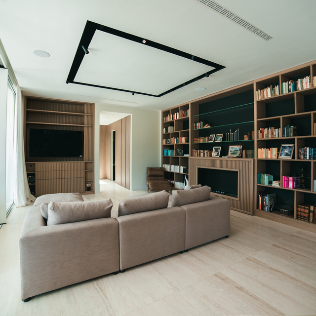 Modern living room with modular sofa, floor-to-ceiling wooden bookshelves, fireplace, and a rectangular black ceiling light frame.