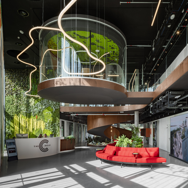 The Circle building lobby with Artemide sinuous LED pendant lights, a cylindrical green wall installation, red curved sofa, and lush vertical gardens