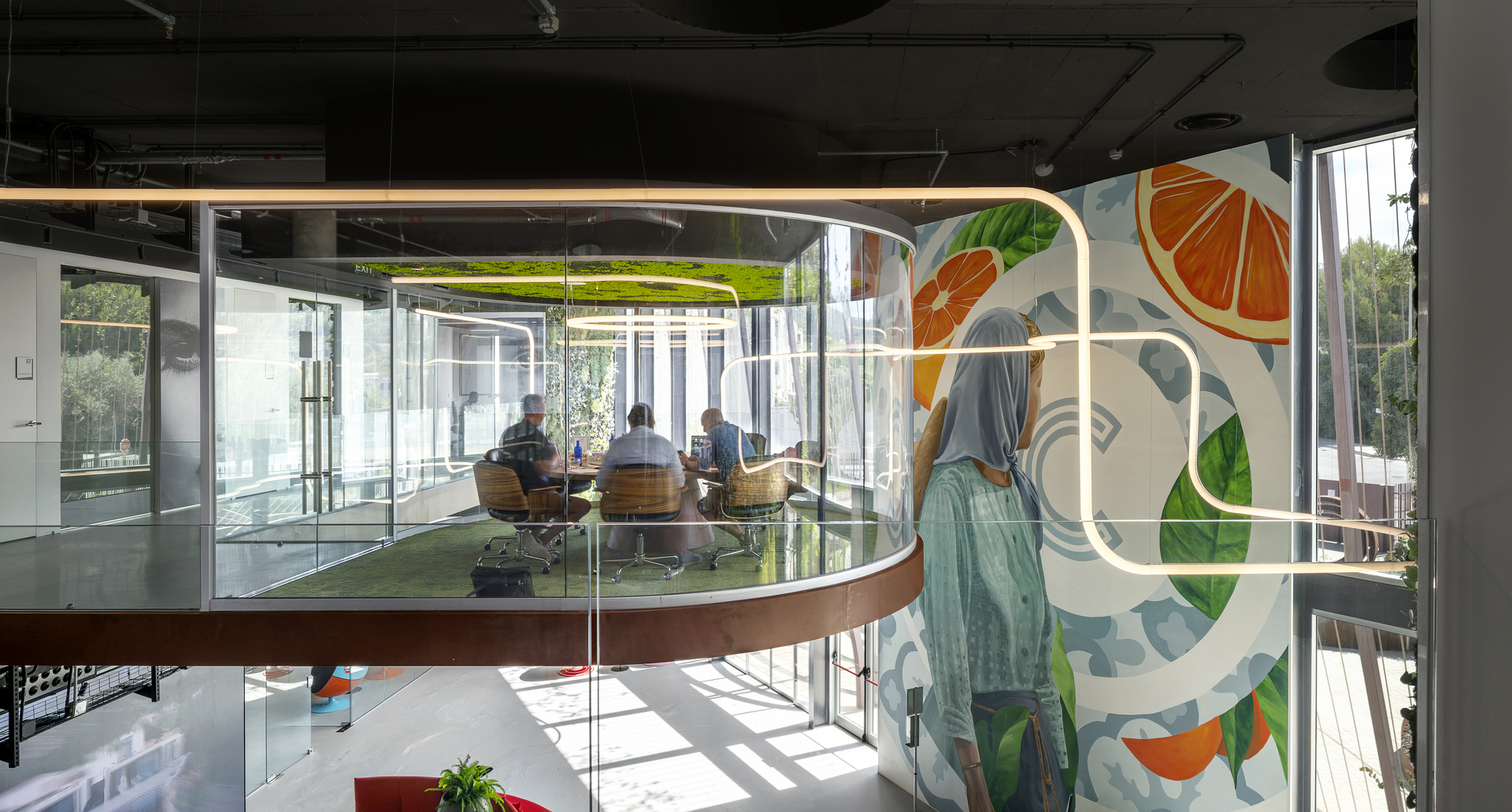 Modern office meeting room with curved glass walls, vibrant fruit mural, and warm Artemide neon-style linear lighting overhead.