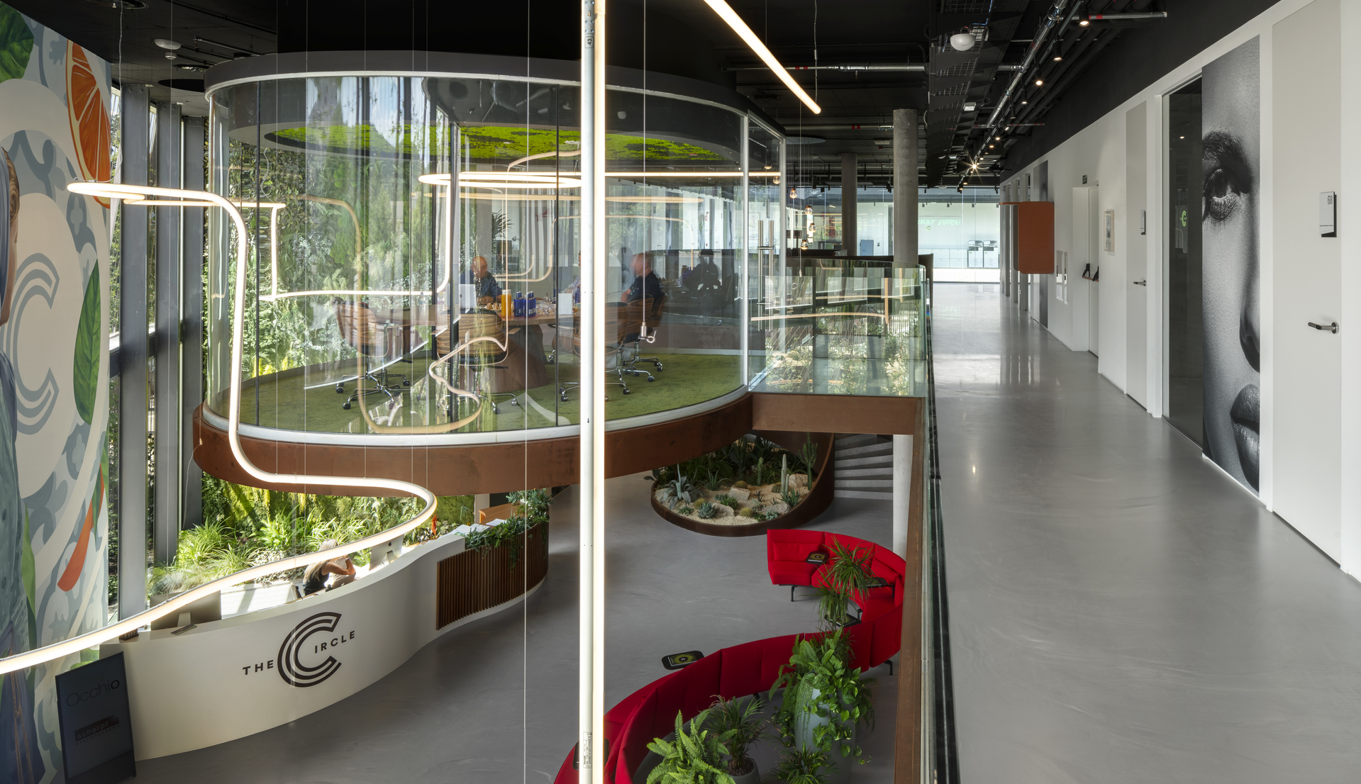 Modern office interior with curved glass partitions, biophilic design, red seating, and Artemide linear pendant lights illuminating the space.