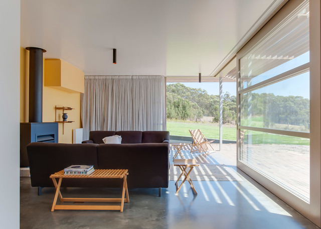 Modern living room with dark sofa, wood coffee table, and a slim wall-mounted Artemide lamp near large windows overlooking green landscape