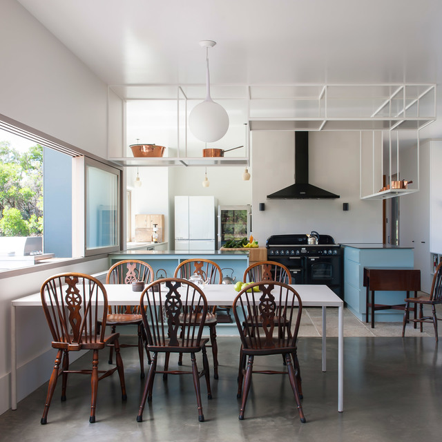 Kitchen-dining area with Artemide globe pendant lamp over white table, Windsor chairs, blue cabinets, and black range cooker.