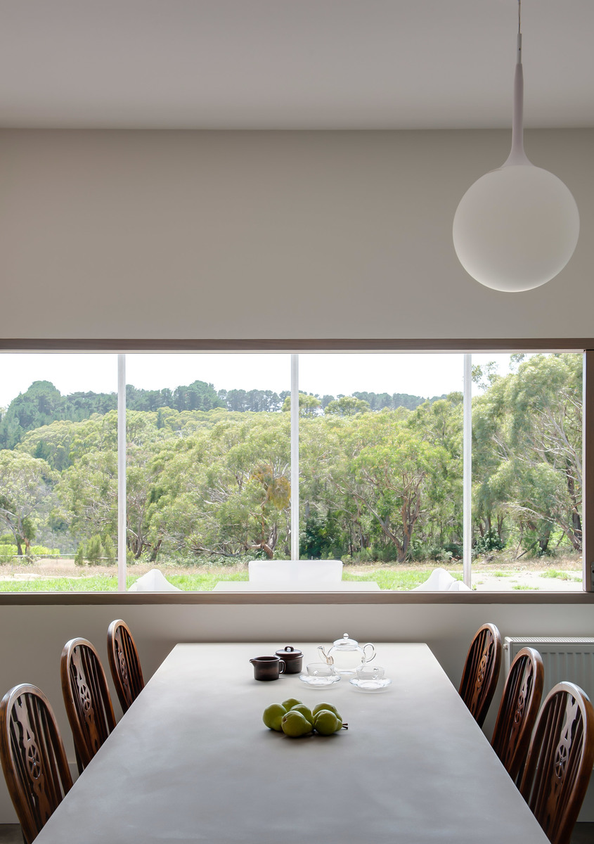 Dining room with white spherical pendant lamp over a long table, wooden chairs, and a wide window overlooking lush green trees