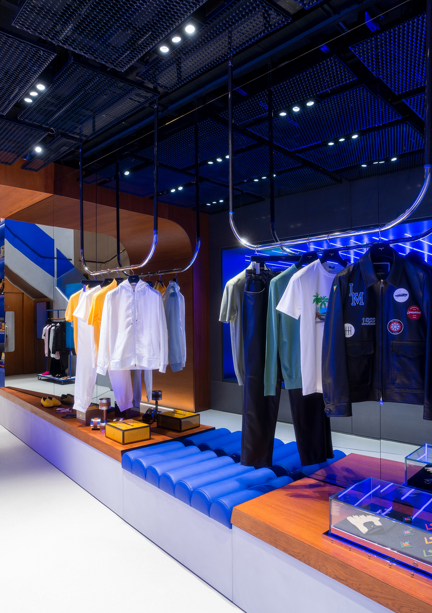 Modern retail store with Artemide recessed spotlights and blue neon accent lighting illuminating clothing displays on hanging racks.