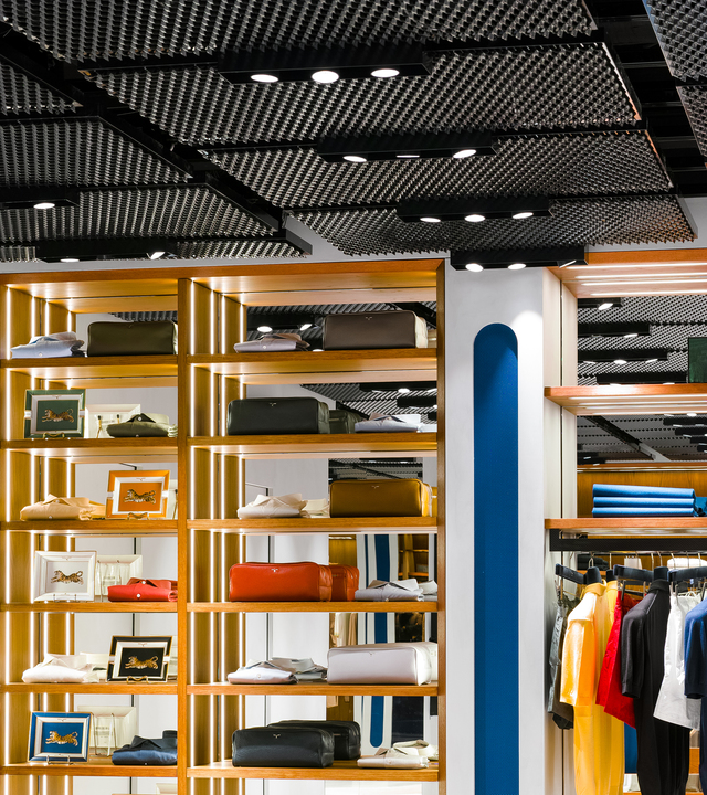 Retail store interior with recessed spotlights on textured black ceiling illuminating wooden shelves displaying luxury goods and clothing.
