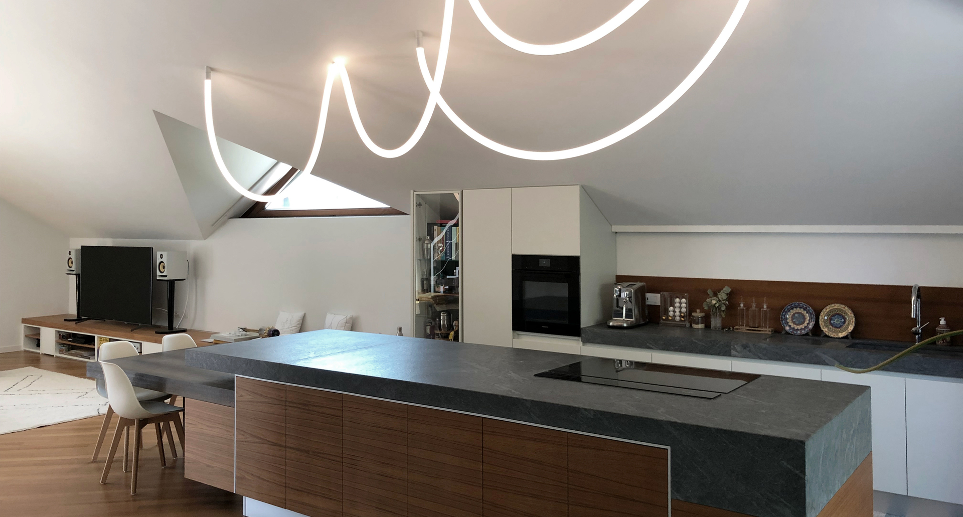 Modern kitchen with a sculptural Artemide LED pendant light featuring fluid, looping white tubes suspended from a sloped ceiling.