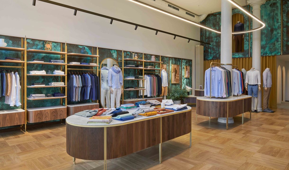 Elegant menswear boutique with Artemide circular LED ring pendant light illuminating walnut display tables and gold-framed clothing shelves