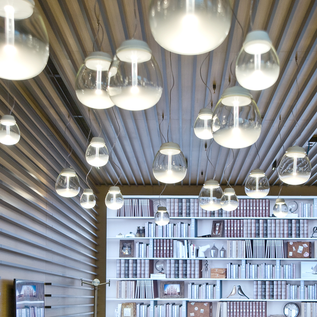 Multiple Artemide Empatia pendant lamps with clear glass globes and white diffusers hang from a slatted ceiling above a library.