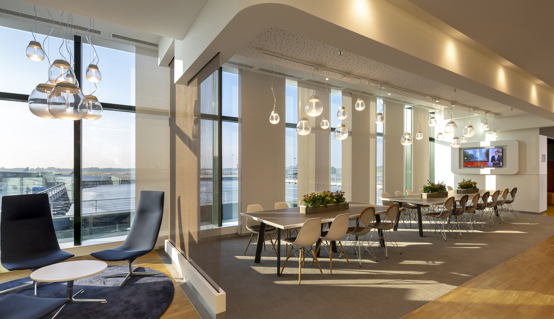 Modern office lounge with Artemide pendant lights featuring glass globe shades, floor-to-ceiling windows, dining area, and contemporary furniture.