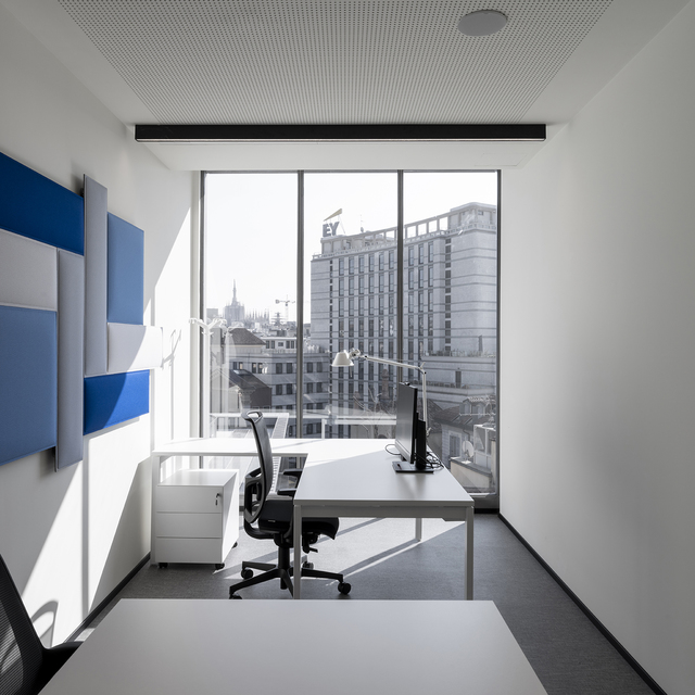 Modern office workspace with Artemide Tolomeo desk lamp on white desk, ergonomic chair, large window with city view