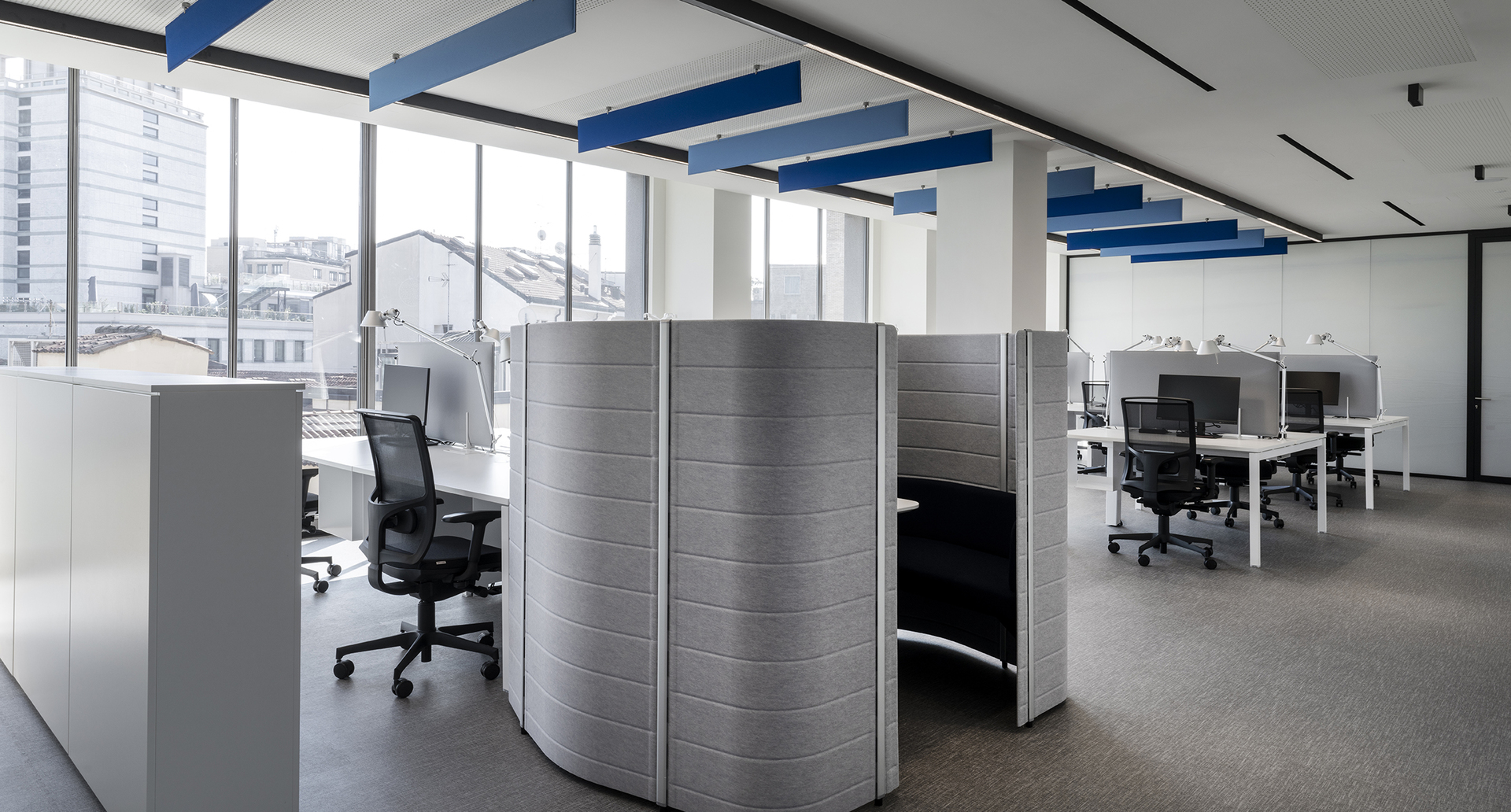 Modern open-plan office with workstations, acoustic pod dividers, ergonomic chairs, and Artemide recessed linear ceiling lights.