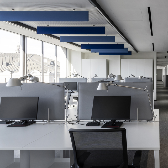 Modern open-plan office with Artemide Tolomeo desk lamps on workstations and blue acoustic panels suspended from ceiling