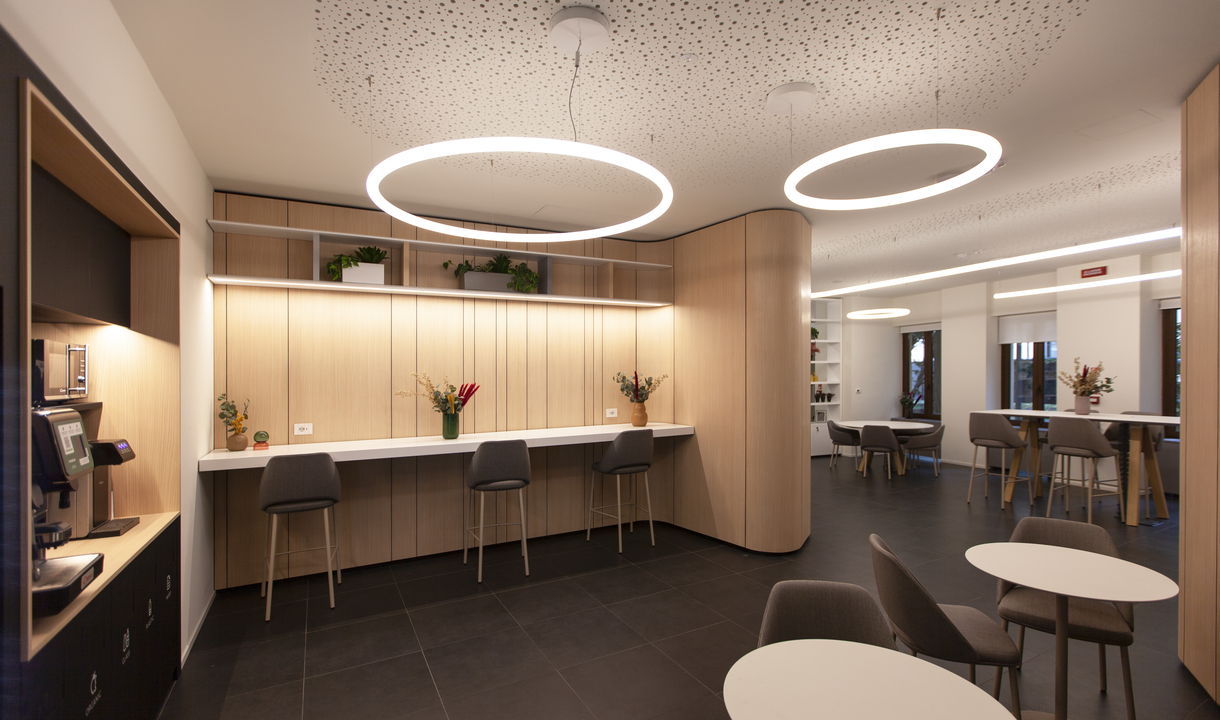 Modern lounge with two large circular LED pendant lights illuminating a wood-paneled counter with bar stools and seating area.