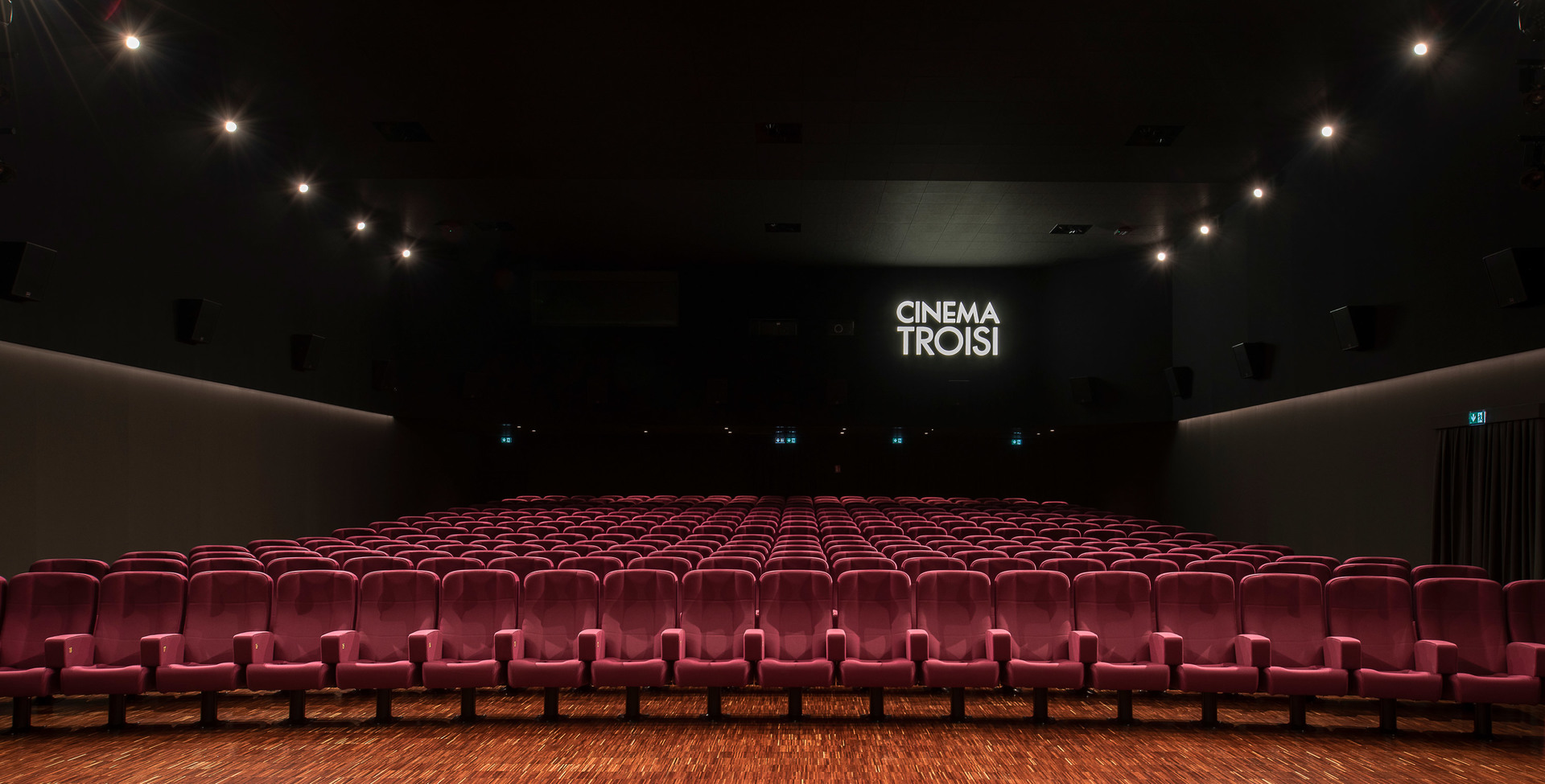 Cinema Troisi auditorium with red velvet seats and Artemide spotlights illuminating the ceiling above the screen.