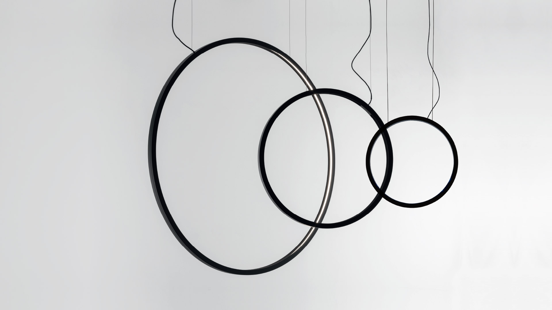 Artemide 'O' outdoor floor lamp: circular black metal ring illuminating a rustic stone wall at night, surrounded by garden greenery