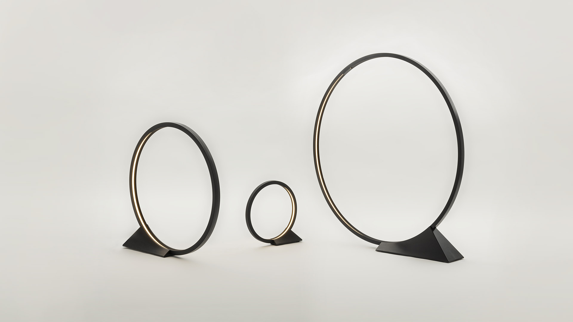 Artemide 'O' circular floor lamp glowing beside a dark garden pool at night, its ring shape reflected in the still water