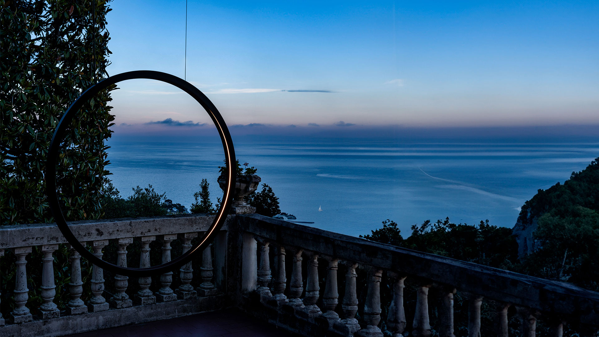 Two Artemide 'O' outdoor floor lamps with circular LED rings in dark finish, placed beside a pool at dusk