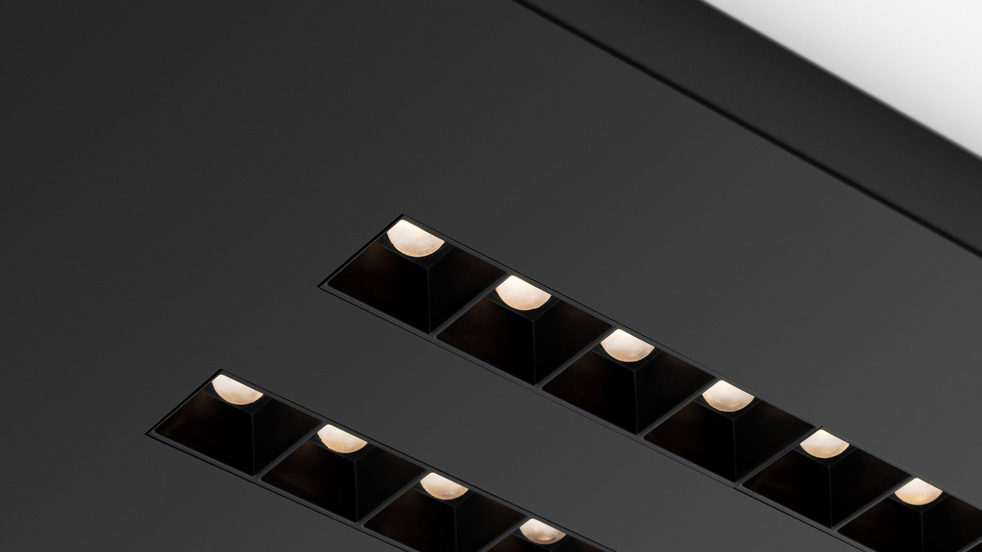 Two recessed linear ceiling fixtures A.39 Refractive Square by Artemide, with multiple square black modules emitting warm white light