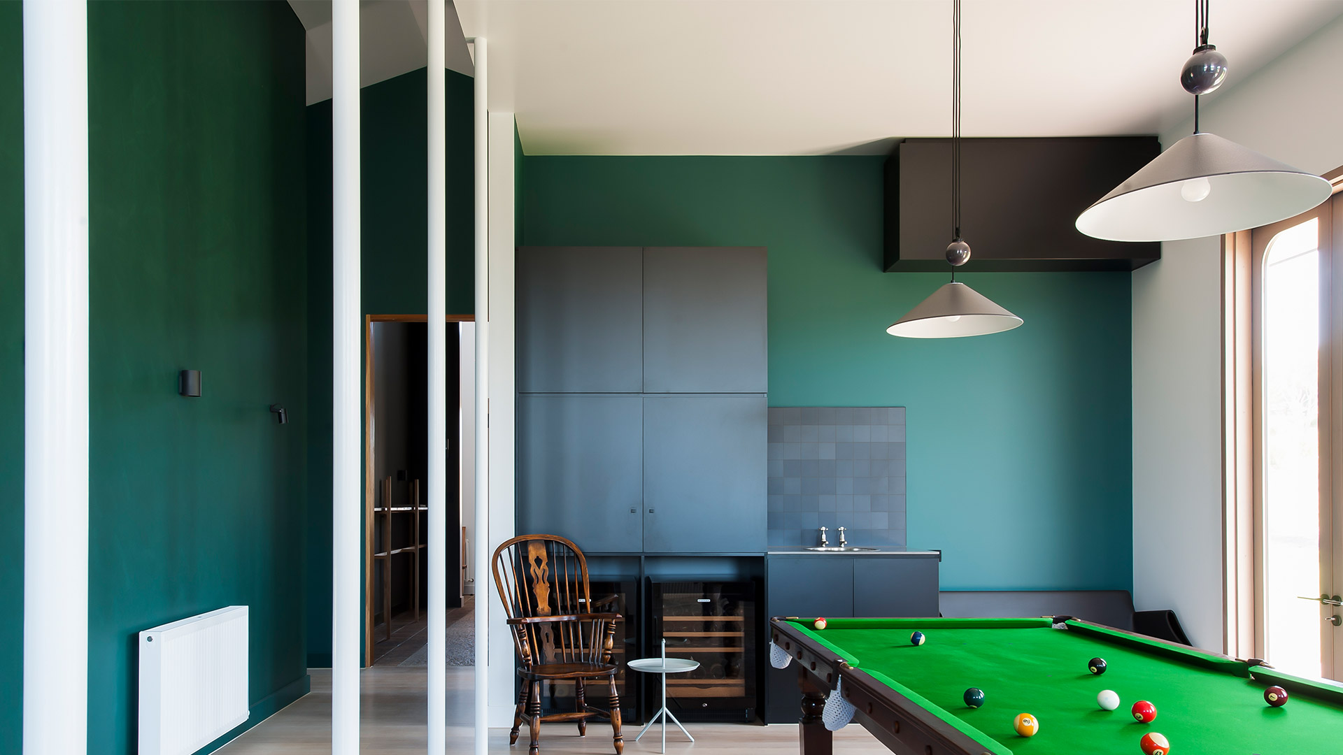 Billiard room with green walls featuring two Artemide Aggregato pendant lamps with grey conical shades and pulley mechanism
