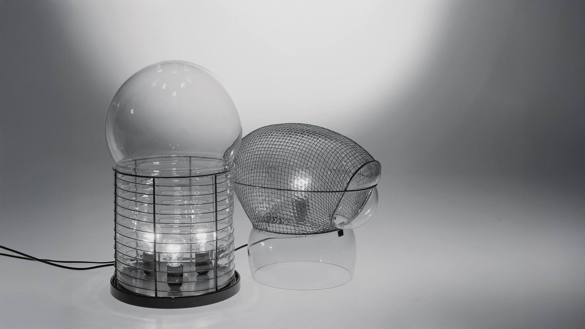 Artemide Alcinoo table lamp with clear glass globe diffuser atop a cylindrical ribbed metal cage structure with copper base