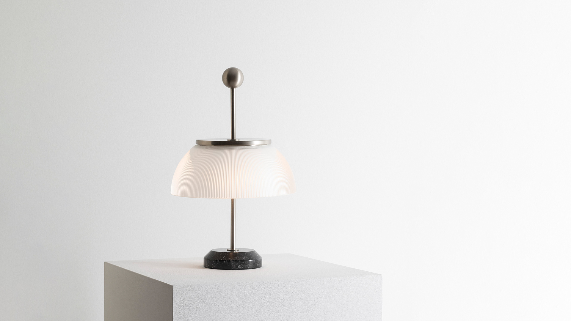 Artemide Alfa table lamp with white dome diffuser and metallic stem on a desk with books, a horse figurine, and framed artwork.