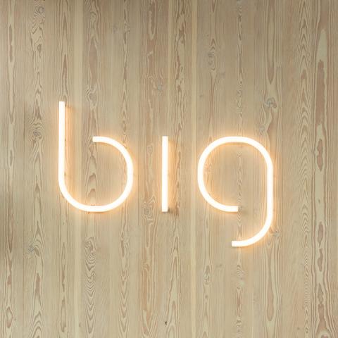 Artemide Alphabet of Light LED letters spelling 'big' in warm white light, mounted on a light wood panel wall