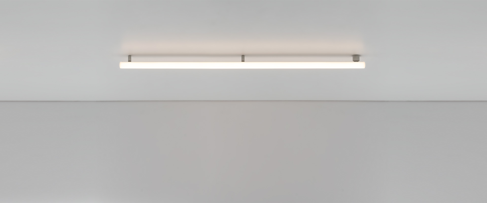 Modern office with open workstations and a glass meeting pod featuring Artemide Alphabet of Light Linear fixtures on yellow walls.