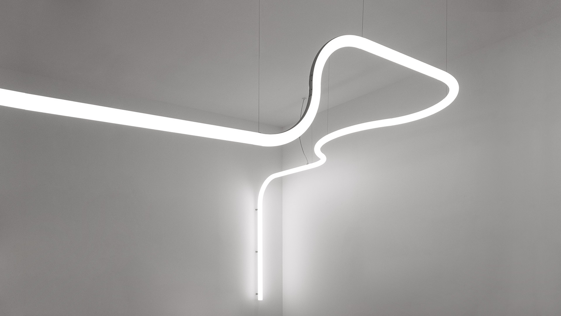 Artemide Alphabet of Light System: glowing white LED tubes forming shapes on wall, with two black circular desk lamps on white pedestal