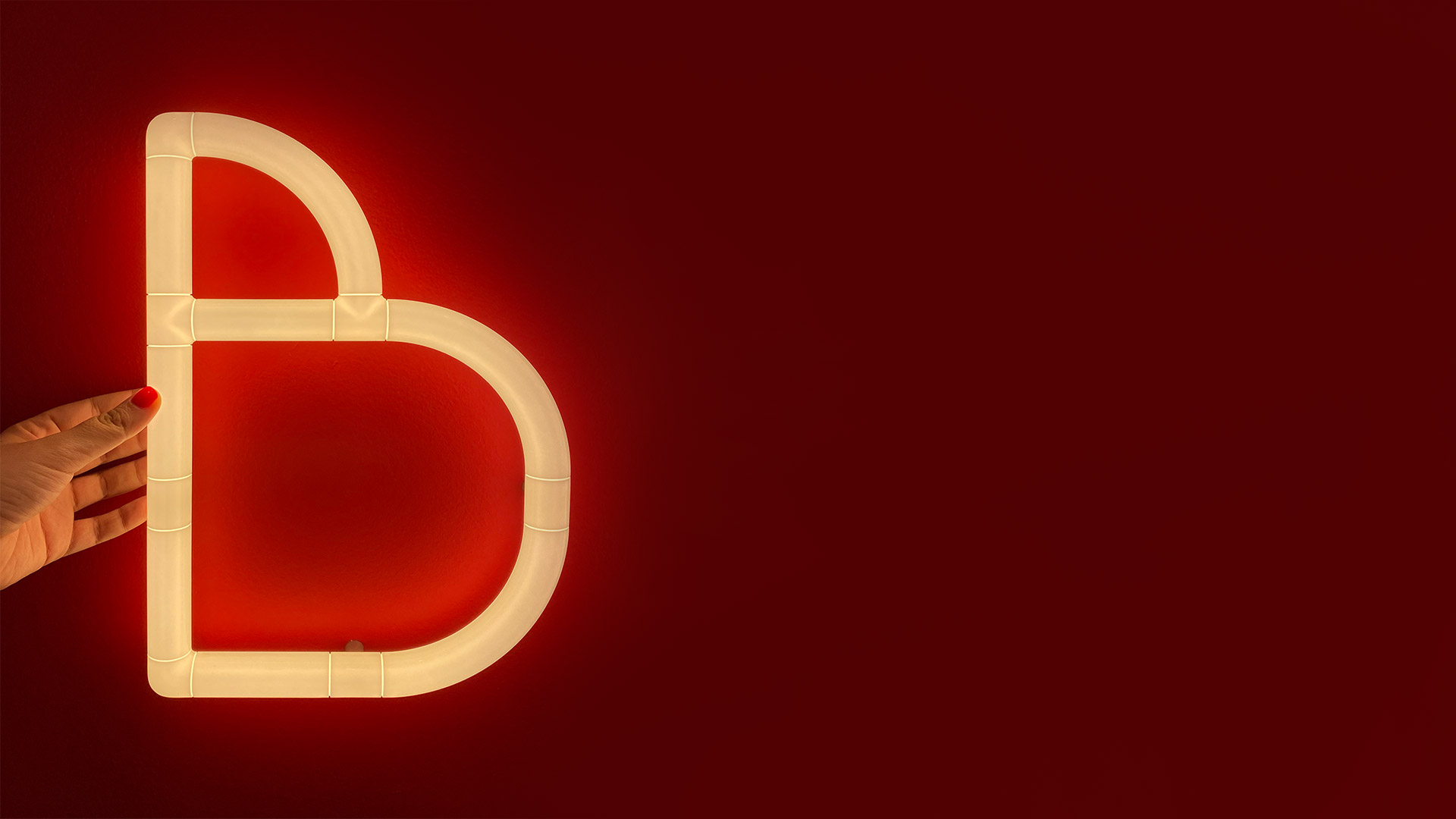 Glowing neon-style 'BIG' letters from Artemide Alphabet of Light Mini on a red wall, beside a small table with potted plants
