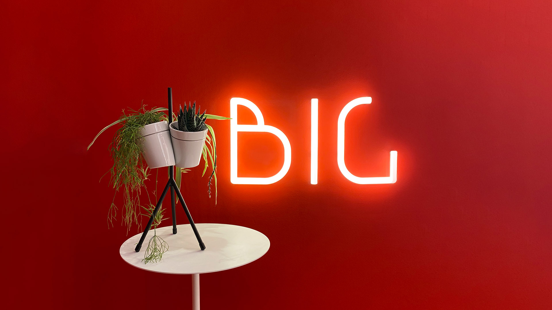 Hand holding a glowing letter B from Artemide Alphabet of Light Mini, warm red illumination on dark red background