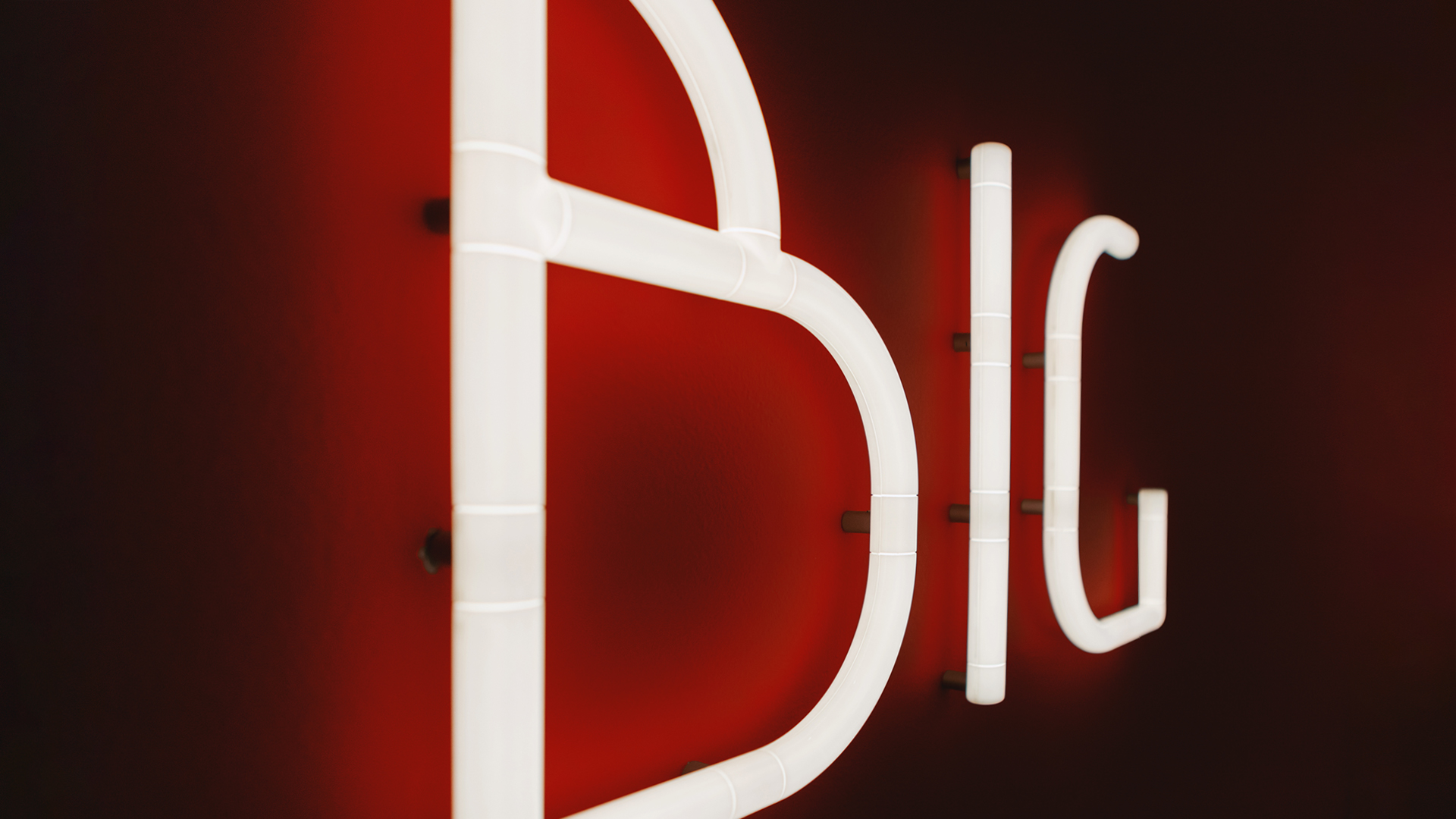 Illuminated white neon-style letters spelling 'BIG' mounted on a red wall, from Artemide Alphabet of Light Mini collection