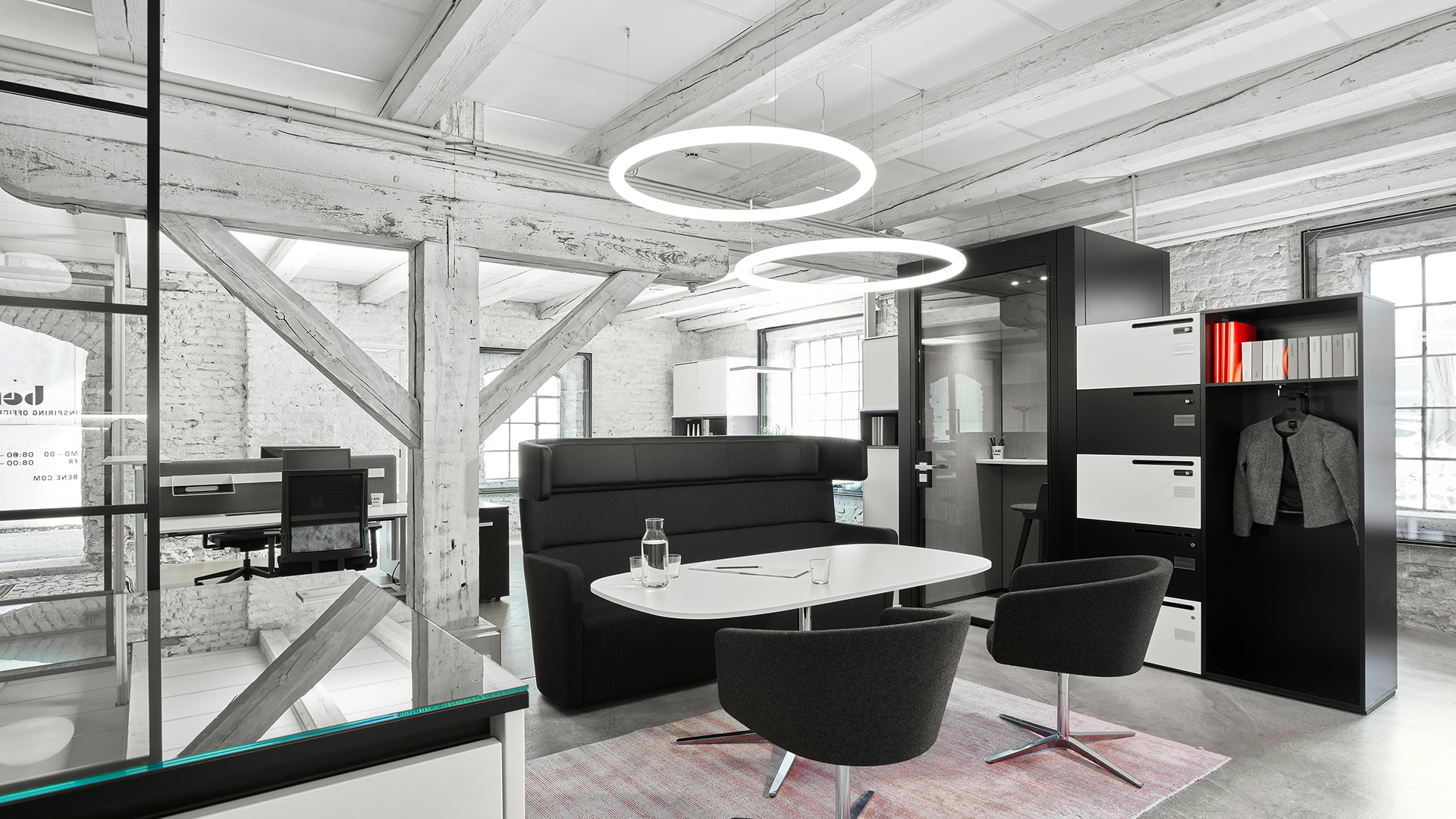 Three Artemide Alphabet of Light Circular pendant lamps in different sizes suspended from an industrial ceiling above a decorated wall.