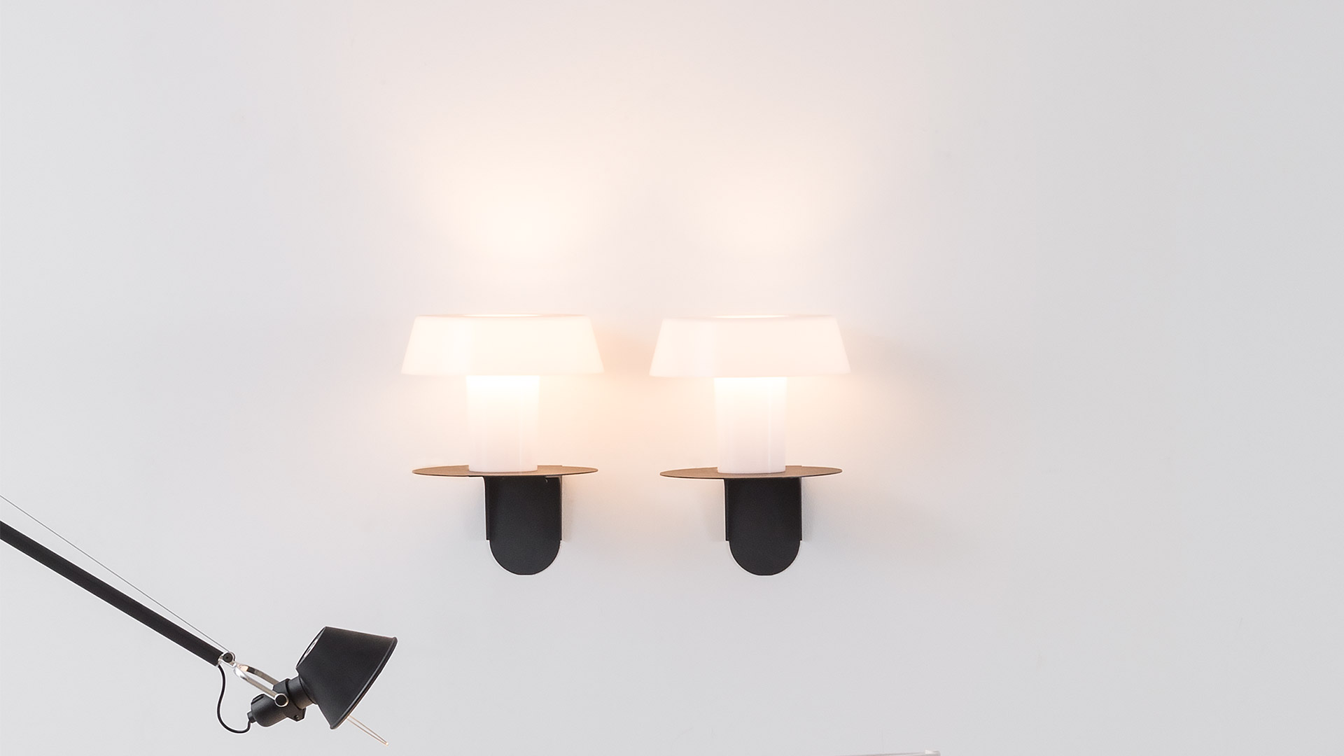 Two Artemide Amami wall sconces with white diffusers and dark bases mounted on a white wall, emitting warm light
